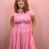 A woman wearing a pink tiered short-sleeve button-up dress, standing against a solid pink wall.