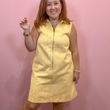 A woman modeling a sleeveless yellow pinstriped mini dress with a front zipper, standing against a solid pink wall.