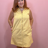 A woman modeling a sleeveless yellow textured dress with a front zipper and pockets, standing against a pink wall.