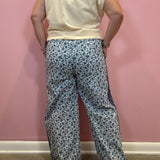 A person shown from the back wearing wide-leg pants with a blue and white floral pattern, paired with a cream sleeveless top, standing against a pink wall.