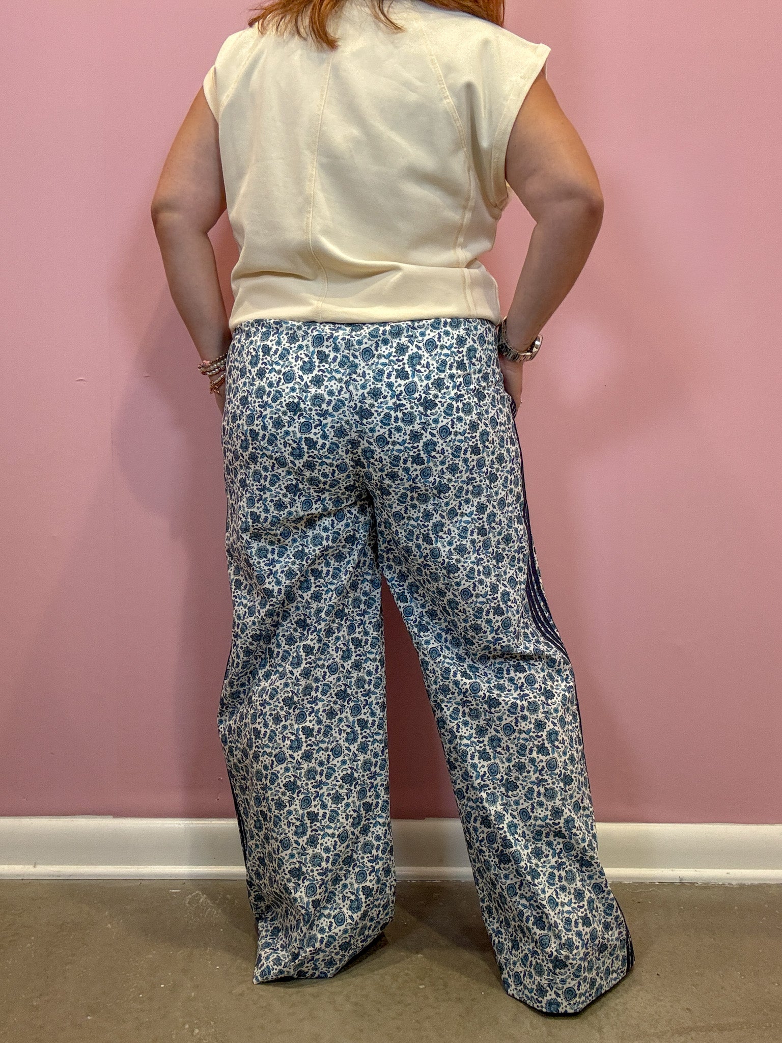 A person shown from the back wearing wide-leg pants with a blue and white floral pattern, paired with a cream sleeveless top, standing against a pink wall.