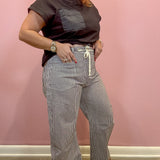 A woman modeling a dark brown short-sleeve t-shirt with a chest pocket and high-waisted, wide-leg gray pinstriped pants with a cream drawstring, standing against a pink wall.