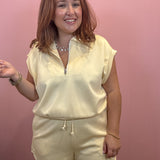 A woman modeling a cream-colored two-piece loungewear set consisting of a short-sleeve half-zip pullover and matching drawstring shorts, set against a solid pink wall.