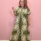 A woman modeling a green and cream block-printed maxi dress against a solid pink wall.