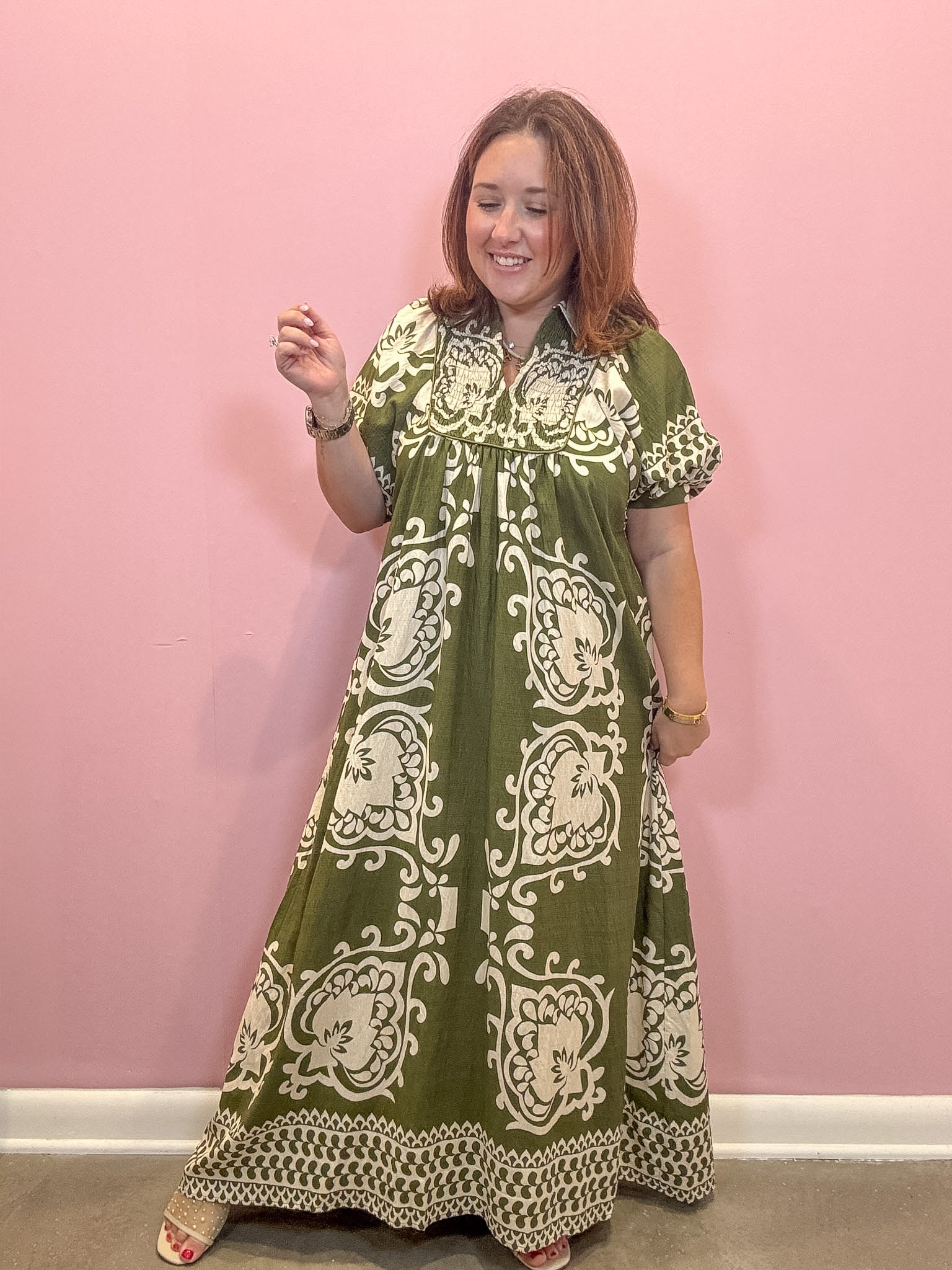 A woman modeling a green and cream block-printed maxi dress against a solid pink wall.