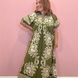 A woman modeling a green and cream block-printed maxi dress against a solid pink wall.