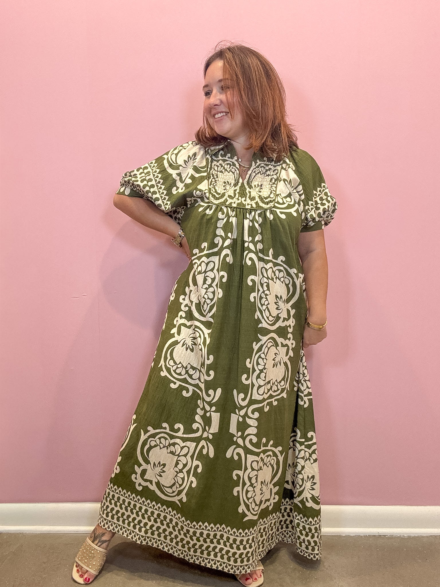 A woman modeling a green and cream block-printed maxi dress against a solid pink wall.