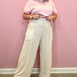 A woman stands against a pink wall wearing a light pink short-sleeve top and cream wide-leg pants with a drawstring waist and frayed hems.