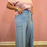 A person wearing a light pink short-sleeve knit top and light blue wide-leg denim pants with raw hems, standing against a pink wall.