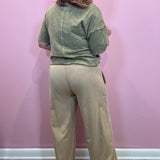 A woman shown from the back wearing a heathered sage green short-sleeve top and beige wide-leg pants, standing against a solid pink wall.