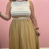 A woman wearing a sleeveless ribbed knit maxi dress with a cream and tan striped bodice and a flowing mustard-gold skirt, standing against a pink wall.