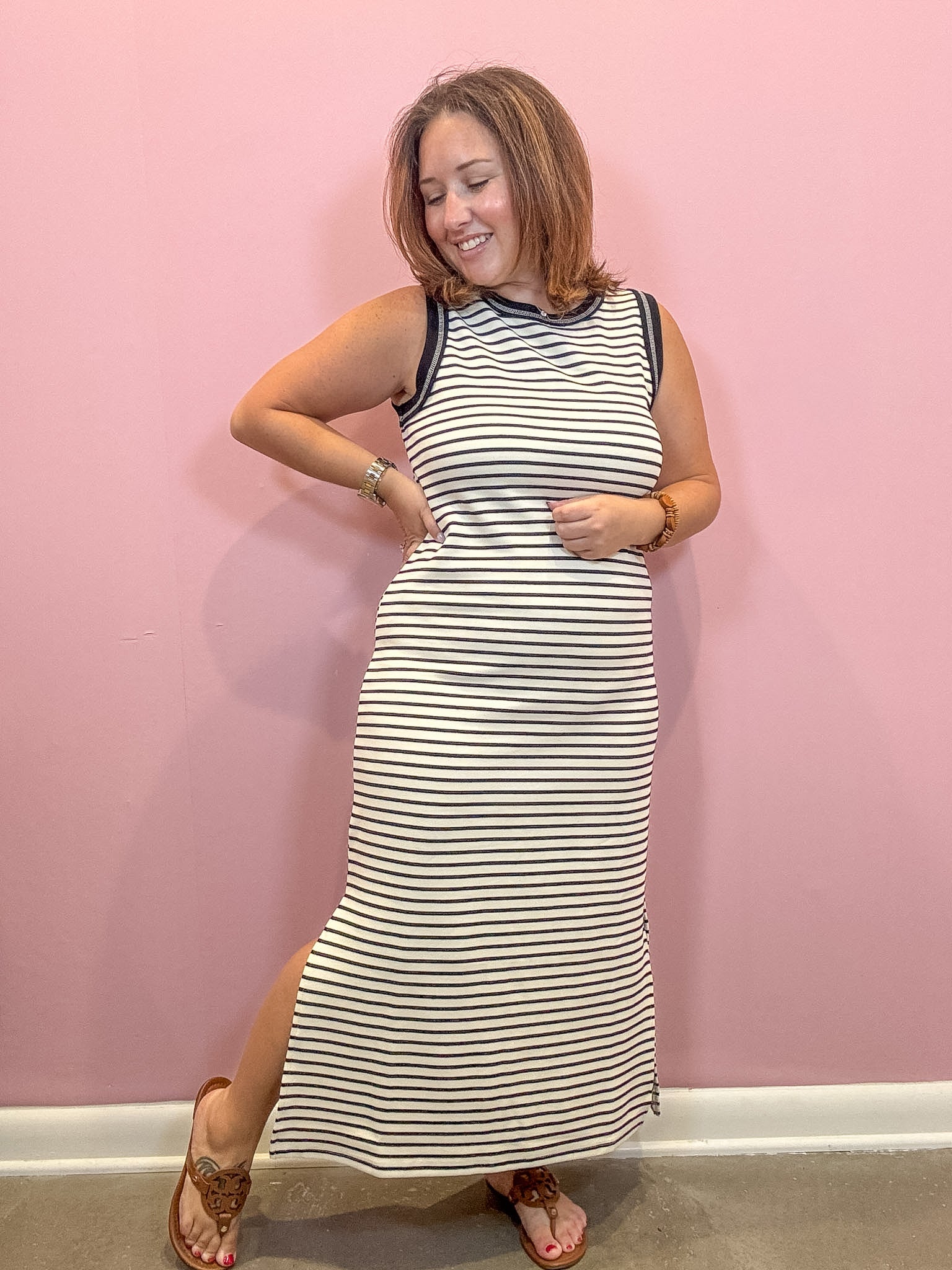 Black and white sleeveless striped midi dress worn by a woman against a pink wall