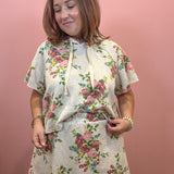 A woman wearing a matching floral-print short-sleeve crop top and shorts set, standing against a solid pink wall.