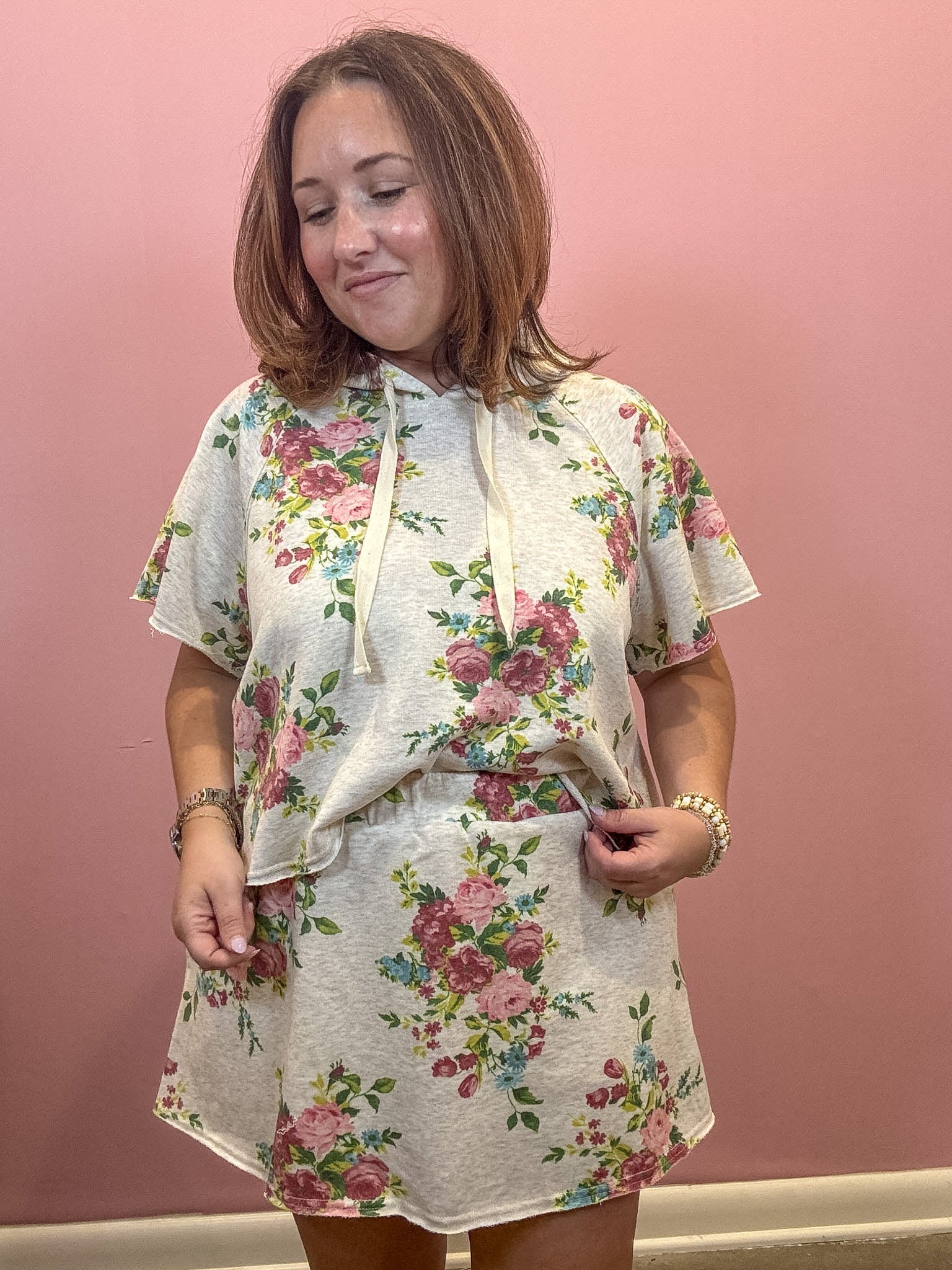 A woman wearing a matching floral-print short-sleeve crop top and shorts set, standing against a solid pink wall.