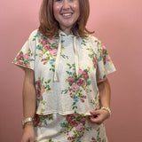 A woman wearing a short-sleeve floral print hoodie and matching mini skirt set, standing against a solid pink wall.