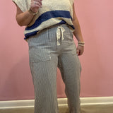 A person wearing a cream textured short-sleeve top with a navy blue horizontal stripe and matching striped drawstring pants, standing against a pink wall.