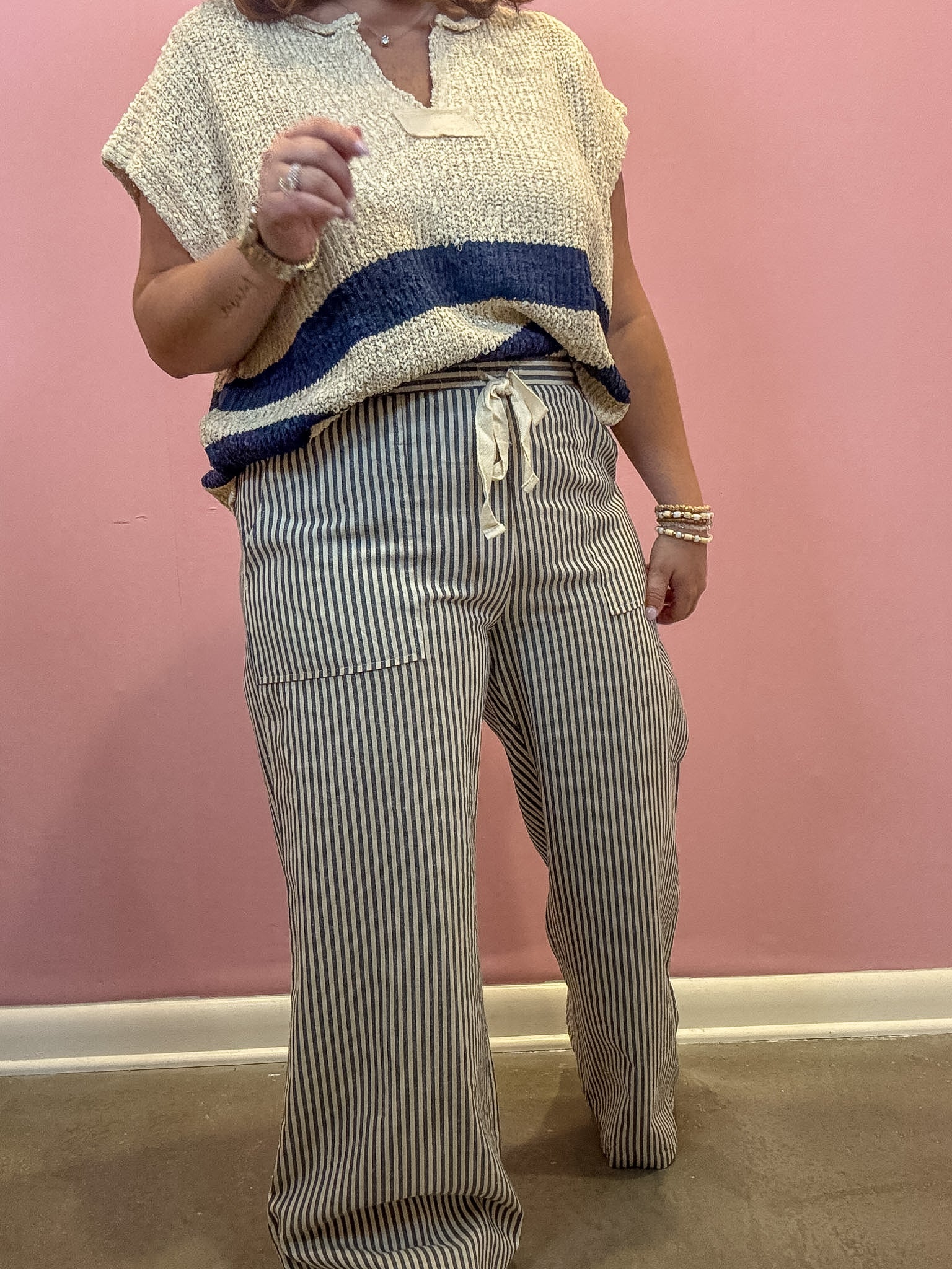 A person wearing a cream textured short-sleeve top with a navy blue horizontal stripe and matching striped drawstring pants, standing against a pink wall.