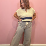 A woman posing in a cream knit short-sleeve top with a navy blue horizontal stripe and matching striped wide-leg pants, standing against a solid pink wall.
