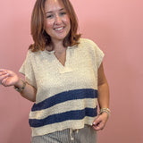 A woman wearing a textured knit top with a cream base and navy blue horizontal stripes, paired with striped pants, standing against a solid pink wall.