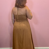 A woman viewed from behind wearing a sleeveless, smocked-bust maxi dress in a warm camel brown color, standing against a solid pink wall.