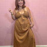 A woman modeling a brown halter-neck maxi dress with a textured bralette-style top, standing against a solid pink wall.