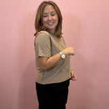 A woman modeling a beige short-sleeve t-shirt and black skirt against a solid pink wall.
