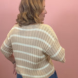 A woman shown from the back wearing a beige and white horizontally striped ribbed knit top, paired with blue jeans, against a solid pink wall.
