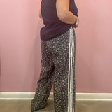 A person shown from the back wearing wide-leg patterned pants with three white side stripes, a dark sleeveless top, and a watch, standing against a pink wall.