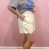 A woman modeling a black and white striped t-shirt with a blue graphic and a cream-colored skirt, standing against a pink wall.