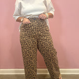 A person wearing leopard-print wide-leg pants and a white top stands against a pink wall, with the pants as the likely product focus.