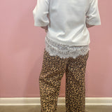 A person shown from the back wearing leopard-print pants and a white top, standing against a pink wall.