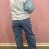 A person shown from the back wearing a white cropped top with a sheer mesh yoke, wide-leg blue jeans, and carrying a blue floral shoulder bag against a pink wall.