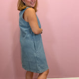 A woman modeling a light blue corduroy sleeveless dress against a solid pink wall.