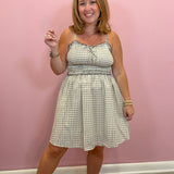 A woman modeling a sleeveless A-line dress with a green and white gingham pattern, standing against a solid pink wall.