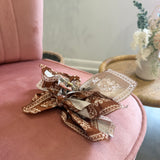 A decorative hair bow made from patterned fabric bands in brown, beige, and white, resting on a dusty pink velvet armchair in a softly styled indoor setting.