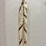 A cream-colored silk scarf with brown stripes, polka dots, and a diagonal stripe pattern, hanging from a gold metal ring against a light beige patterned wallpaper background.