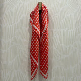 A red and white checkered scarf draped over a gold wall hook against a light beige patterned wallpaper background.