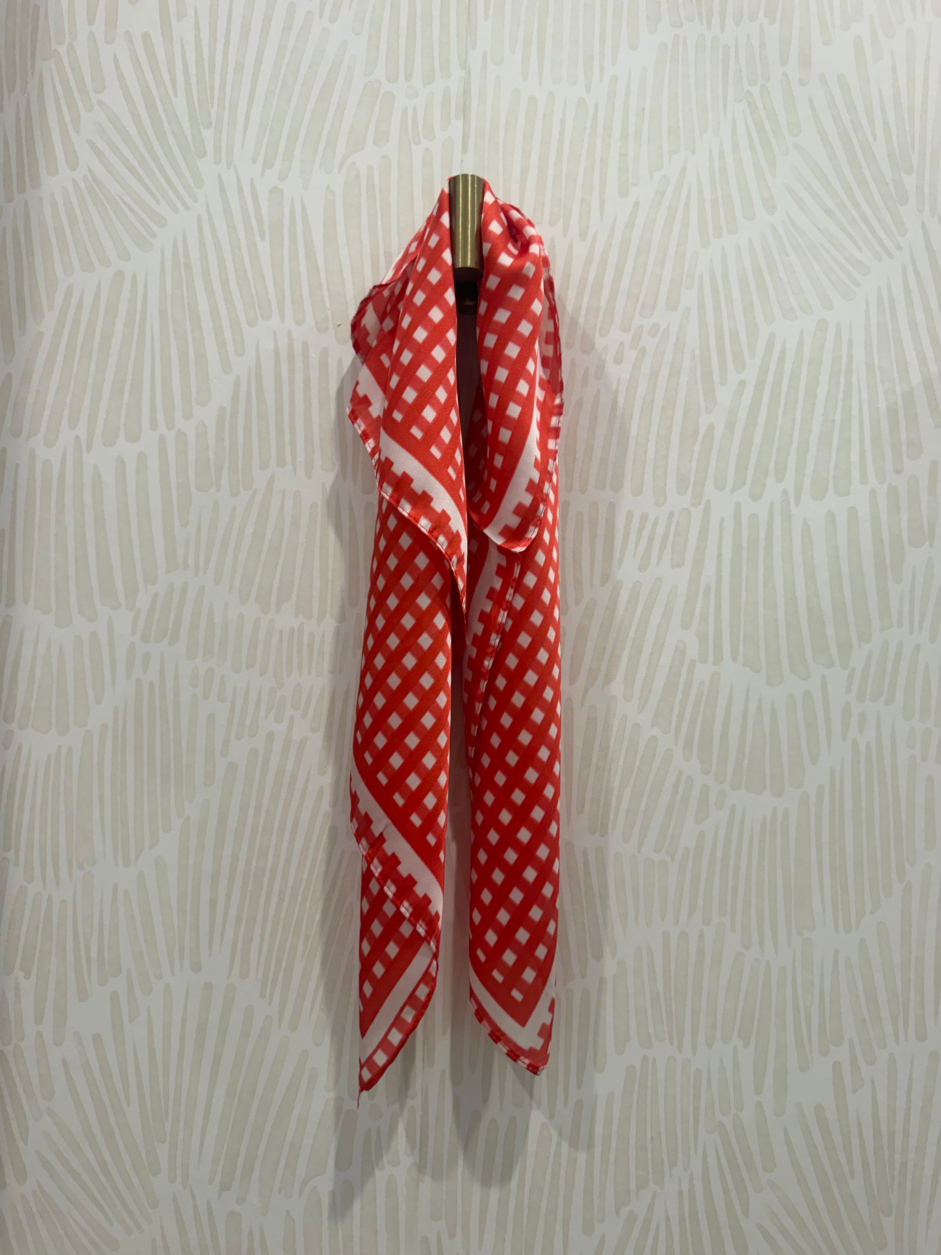 A red and white checkered scarf draped over a gold wall hook against a light beige patterned wallpaper background.