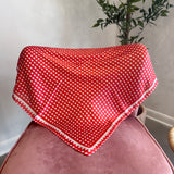 A red and white gingham checkered bandana or scarf draped over a dusty pink velvet armchair in a home setting, with a potted plant and wall visible in the background.
