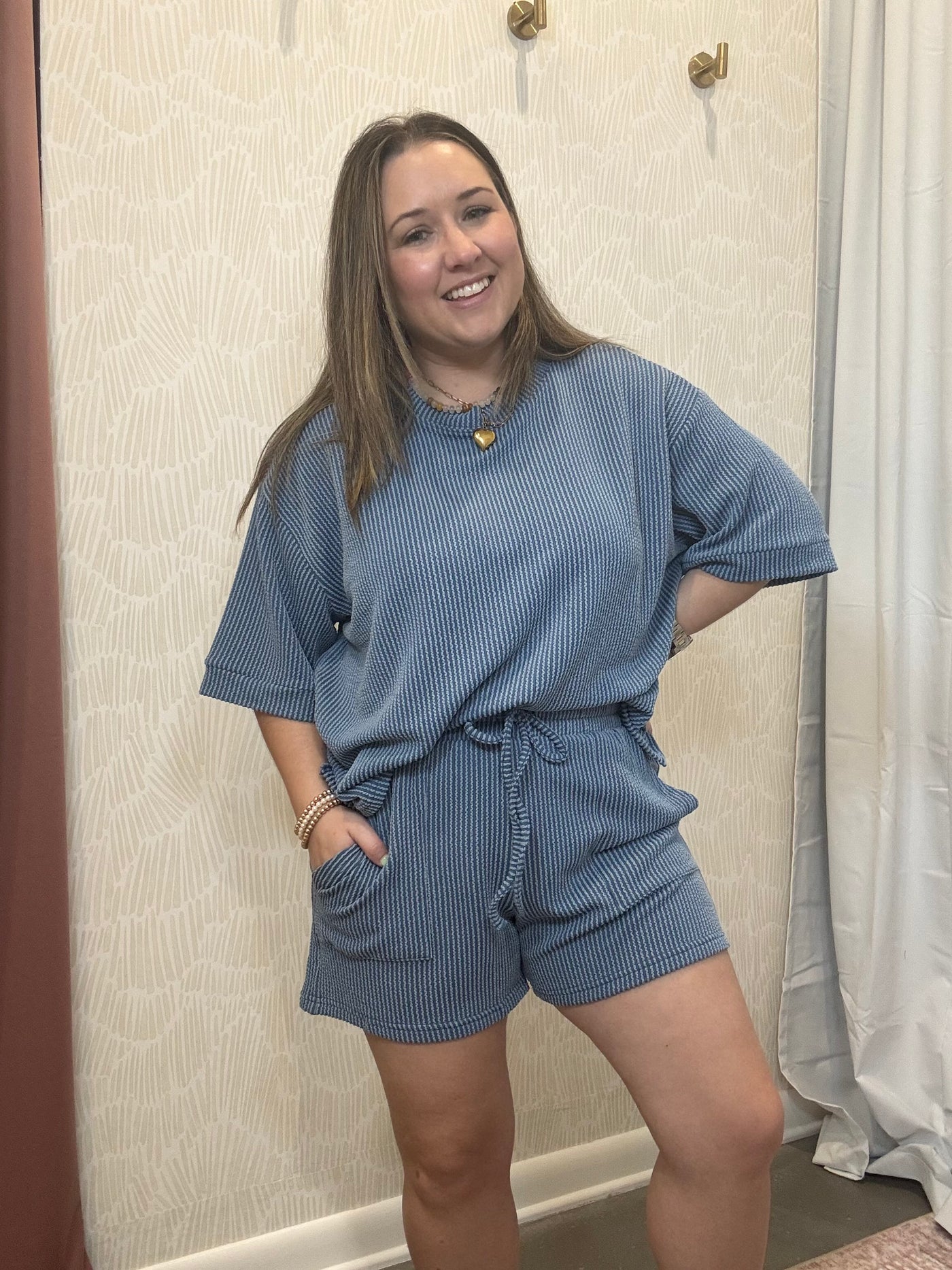 Woman wearing a blue textured outfit standing in front of a neutral wall.