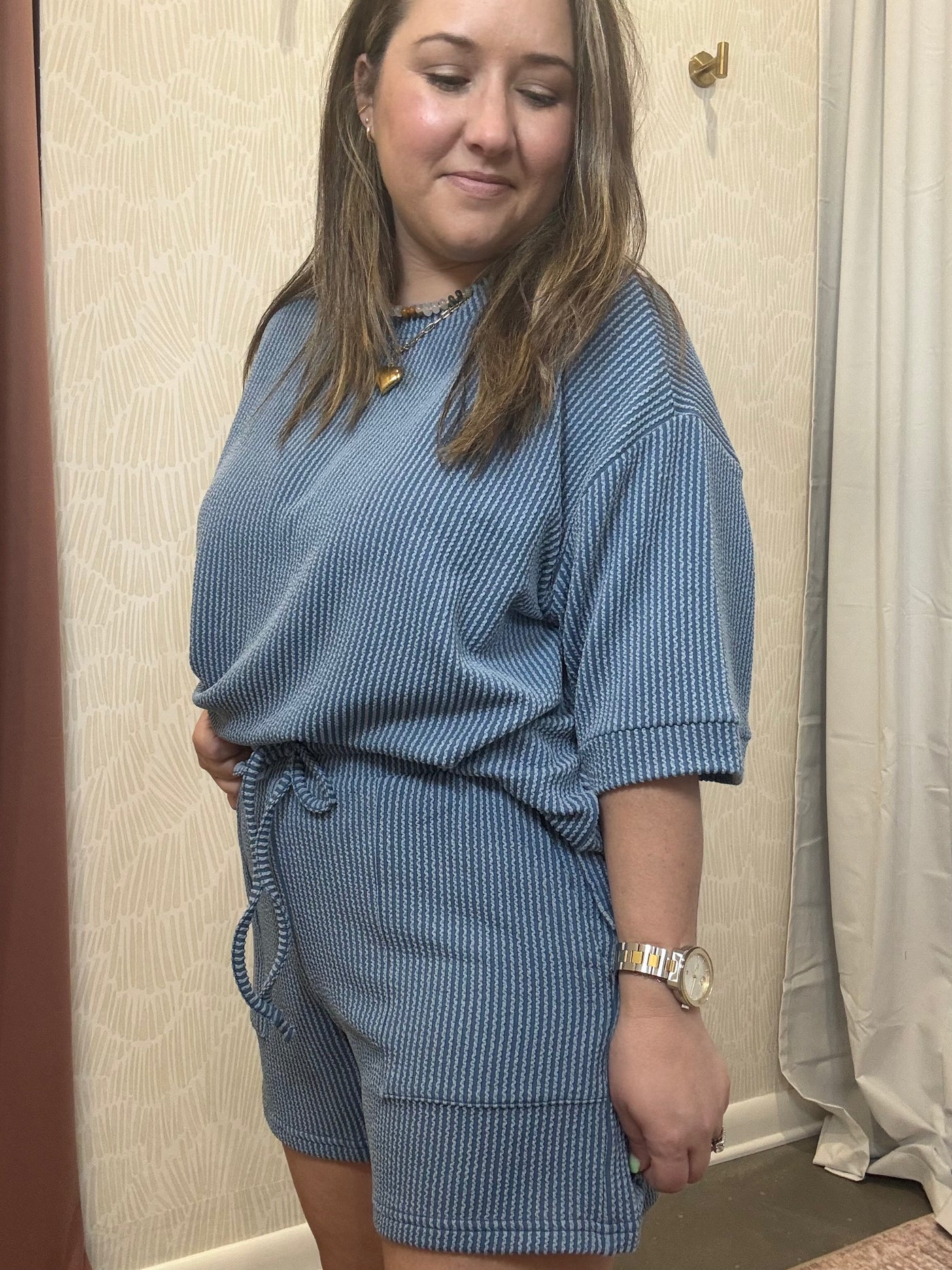 Person wearing a blue ribbed outfit standing in a room with beige walls.