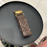 A brown leather belt with a braided woven center and a gold-tone buckle, displayed on a round black side table.