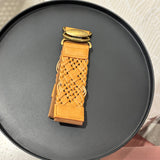 A tan woven leather belt with gold-tone hardware, displayed on a round black surface.