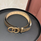 A tan leather belt with a gold-tone interlocking double-O buckle, coiled on a round black tray.