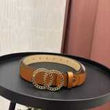 A tan leather belt with a large interlocking double-O chain buckle, displayed on a black round table.