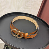A tan leather belt with a large interlocking double-O ring buckle, displayed on a round black tray.