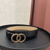 A black leather belt with a large interlocking double-ring buckle in a textured gold-tone finish, displayed on a round black side table.