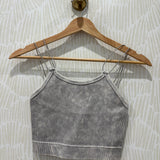 A gray ribbed knit camisole crop top with thin shoulder straps, hanging on a wooden hanger against a light patterned wallpaper background.