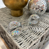 A light blue box of esw beauty ice globes facial tools, featuring an illustration of two pink glitter-coated globes, displayed on a woven table with decorative dried grass and a disco ball in the background.