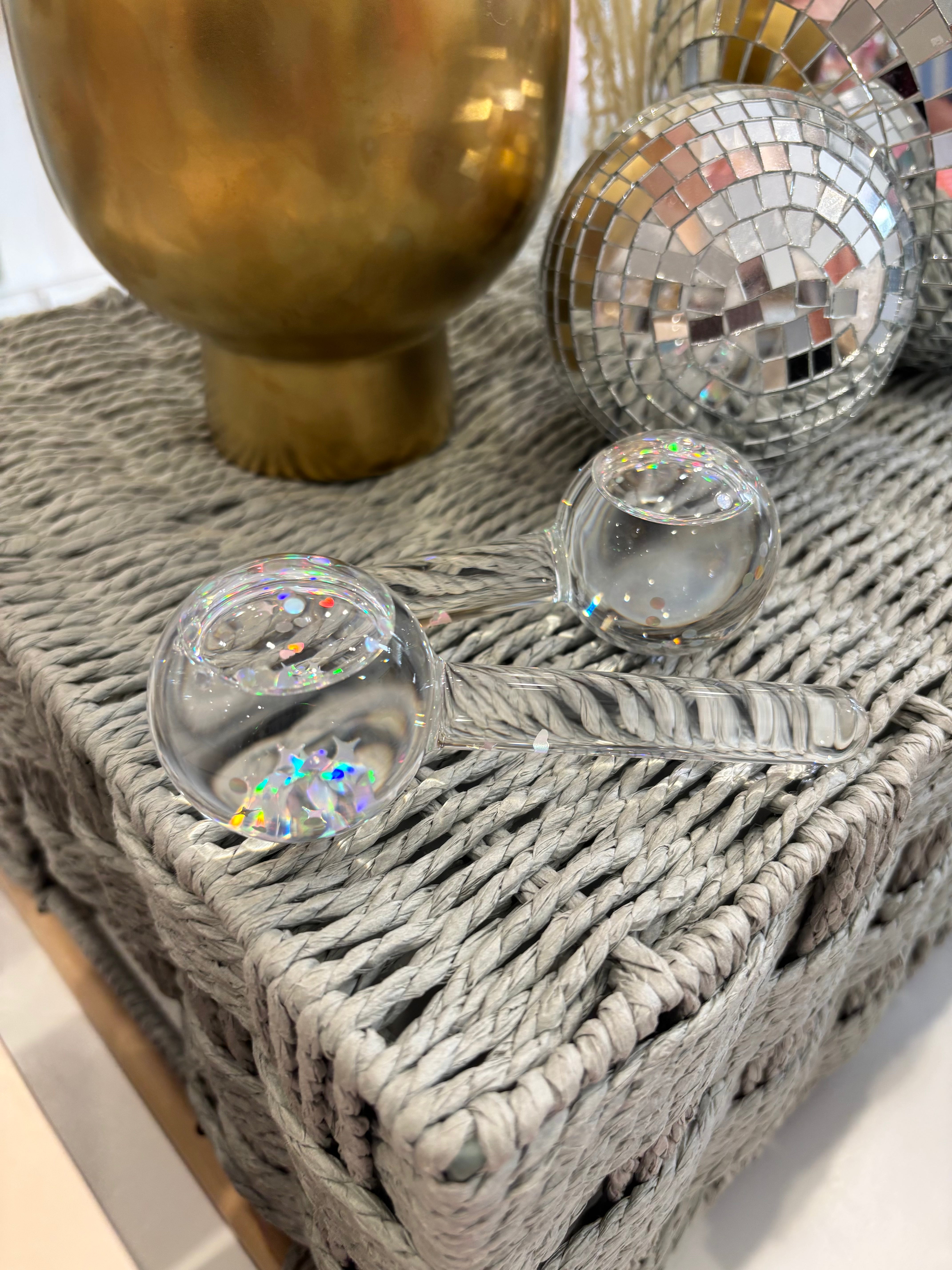 A light blue box of esw beauty ice globes facial tools, featuring an illustration of two pink glitter-coated globes, displayed on a woven table with decorative dried grass and a disco ball in the background.